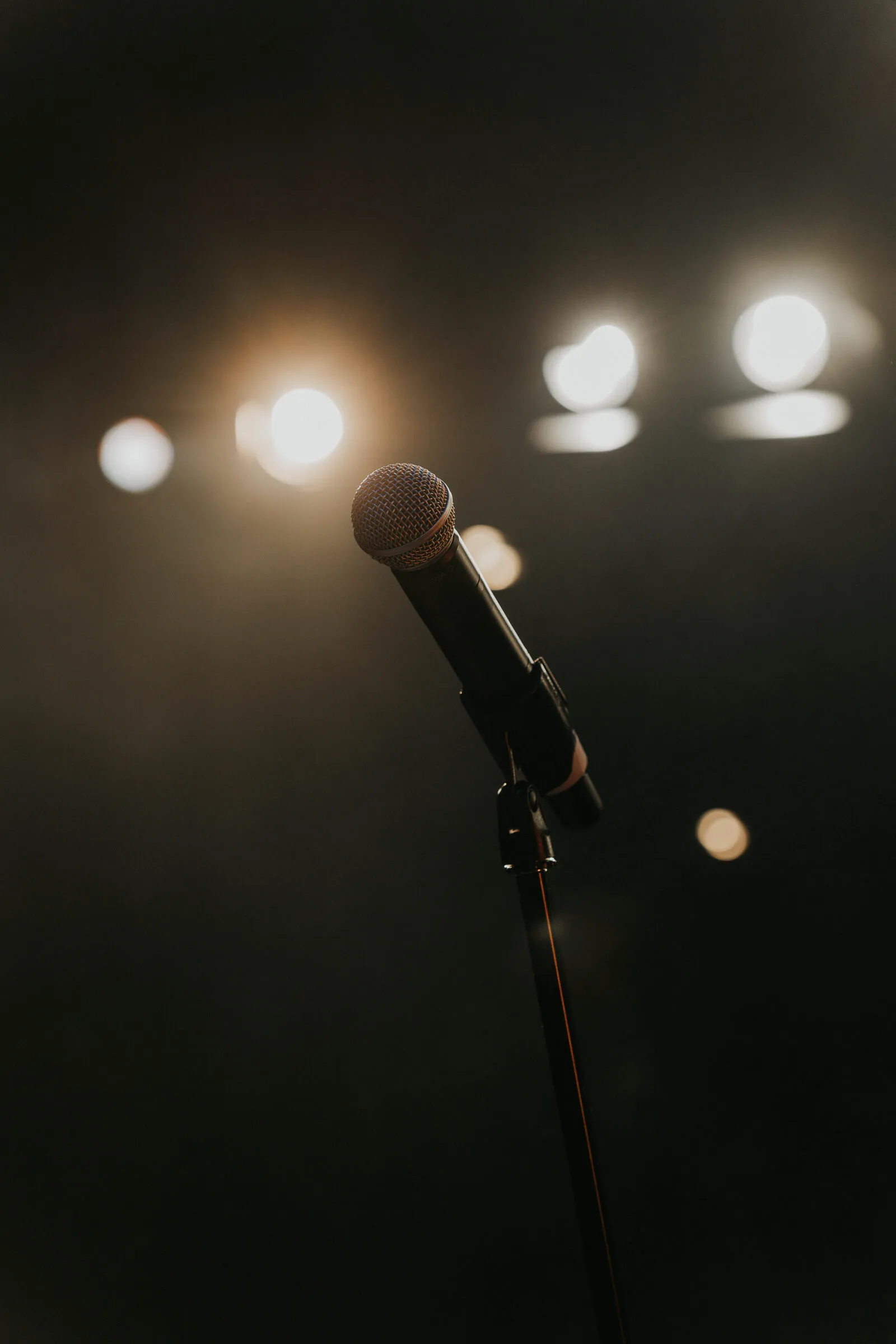 A microphone on its stand against out-of-focus stage lights
