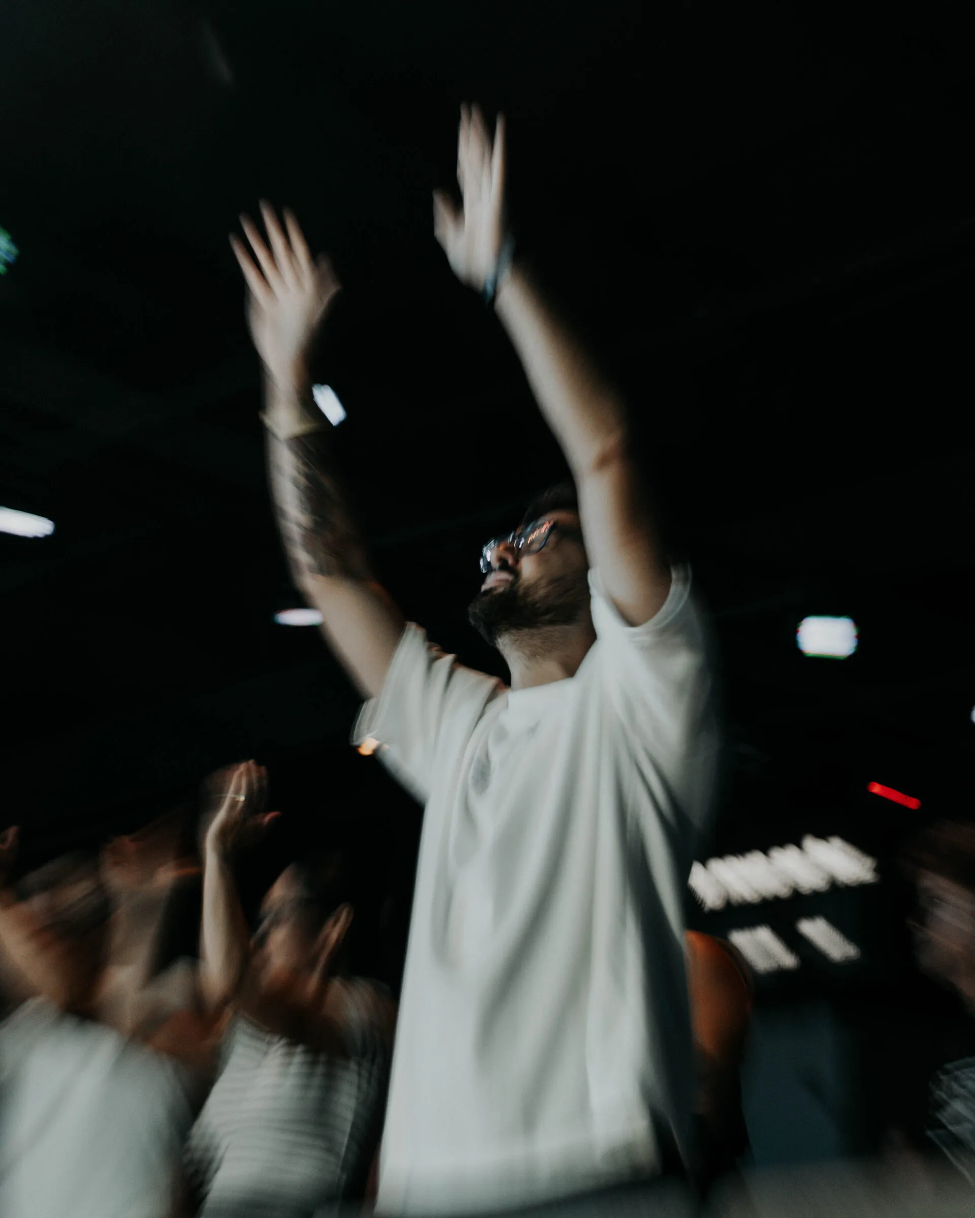 Hands raised in the front row, caught with a dragged shutter so the crowd smears into motion