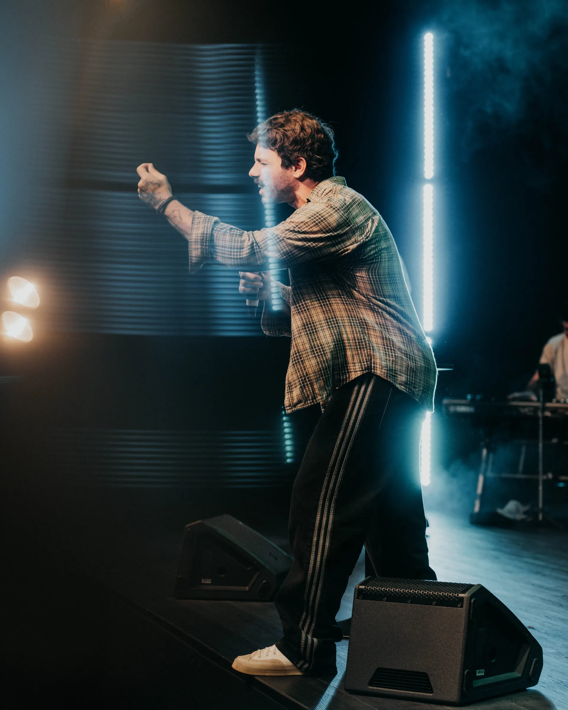 A guitarist reaching upward between vertical bars of stage light